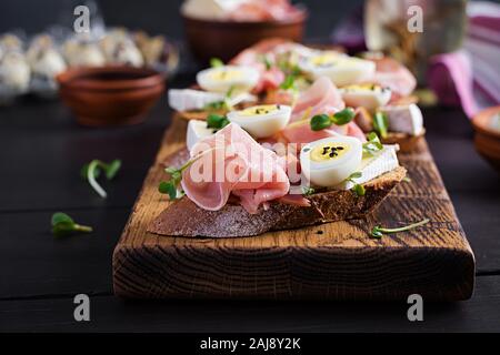 Bruschetta con prosciutto/jamon Italiano tradizionale di antipasto. Delizioso spuntino con pane, formaggio brie e uova di quaglia. Health food, tapas Foto Stock