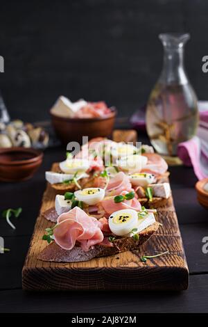 Bruschetta con prosciutto/jamon Italiano tradizionale di antipasto. Delizioso spuntino con pane, formaggio brie e uova di quaglia. Health food, tapas Foto Stock