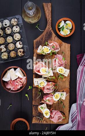 Bruschetta con prosciutto/jamon Italiano tradizionale di antipasto. Delizioso spuntino con pane, formaggio brie e uova di quaglia. Health food, tapas. Vista dall'alto, Foto Stock