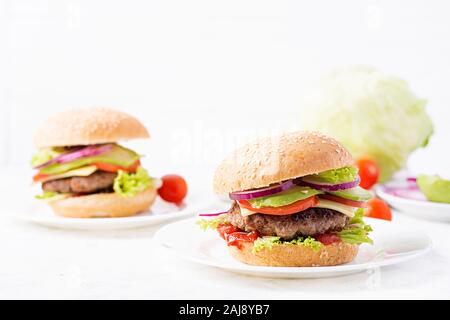 Grande panino - hamburger burger con carne di manzo, avocado, pomodori e cipolle rosse su sfondo chiaro. Cucina americana. Il Fast Food Foto Stock