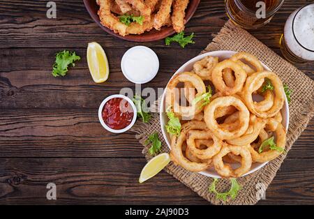 Anelli di cipolla in pastella con salsa di pomodoro e formaggio bastoni. La birra snack. Vista superiore, overhead, spazio di copia Foto Stock