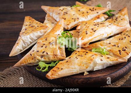 Cibo asiatico. Samsa (samosa) con filetto di pollo e formaggio su sfondo di legno. Foto Stock