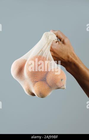 Primo piano di un uomo con un tessile riutilizzabile borsa a rete, utilizzato per acquistare generi alimentari alla rinfusa, pieno di arance, come misura per ridurre l'inquinamento in plastica Foto Stock