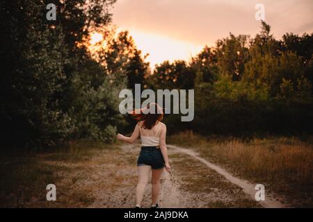 Vista posteriore della giovane donna che cammina su sentiero nella foresta durante l'estate Foto Stock