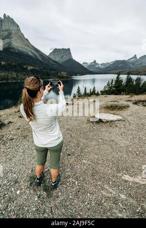 Donna usa il telefono cellulare per scattare foto della vista sulle montagne, Montana Foto Stock