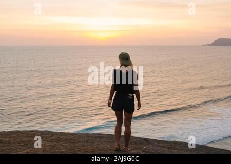 Giovane donna in piedi sulla roccia alla spiaggia al tramonto Foto Stock