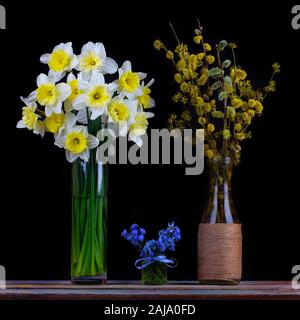 Bouquet di rami fioriti di Willow e sanguinello in un vaso, bouquet di fiore di narciso e bouquet di fiori bluebell in un vaset sul tavolo su un Foto Stock