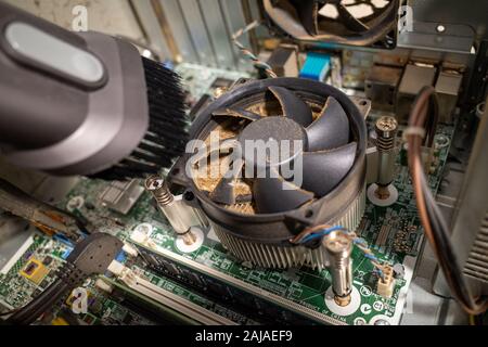 Un molto sporco ventola del computer all'interno di un computer viene pulita con un aspirapolvere Foto Stock