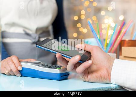 La mano del cliente paga con lo smartphone in negozio utilizzando la tecnologia NFC. Telefono cellulare a pagamento con contatto meno tecnologia. Foto Stock