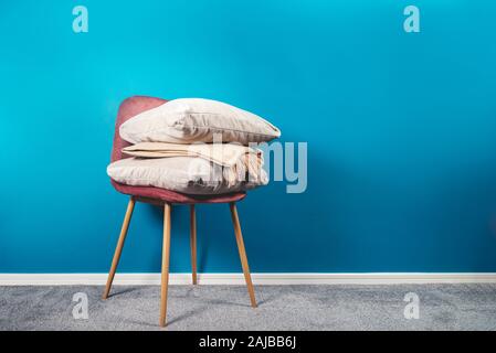 Moderno in velluto rosa sedia con cuscini di colore beige e cashmere buttare sulla parte superiore. La sedia ha le gambe di legno. Sfondo blu Foto Stock