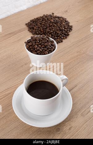 Tazza di caffè con i chicchi di caffè sul tavolo in legno bianco e la parete in mattoni Foto Stock