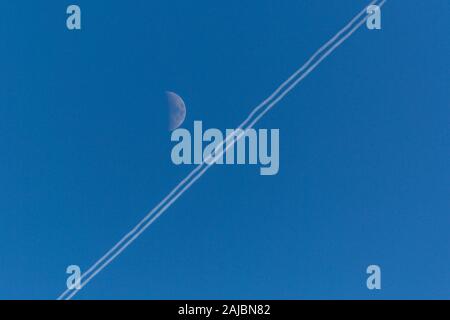 Luminoso cielo blu con il bianco half Moon e condensazione trail su una soleggiata giornata invernale. Foto Stock