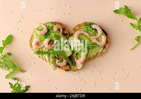 Sano cibo fitness. Aprire il panino con avocado, gamberi e rucola in una forma di cuore. Una corretta alimentazione. Scatto dall'alto. Foto Stock