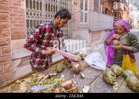 Jodhpur, India - 07 Marzo 2017: un uomo vende noci di cocco sulla strada. Nelle vicinanze sorge una donna e le bevande fresche di latte di cocco. Foto Stock