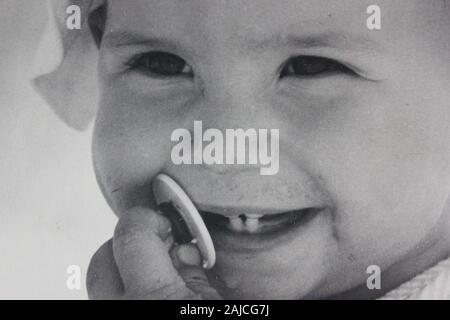 Fine anni settanta fotografia in bianco e nero di una bambina molto felice masticare sul suo succhietto Foto Stock