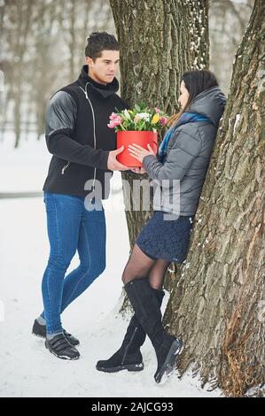 L uomo e le ragazze con confezione regalo rossa con bel bouquet di fioritura rosa, giallo e bianco tulipani e crisantemi bianco con foglie verdi, esterni Foto Stock