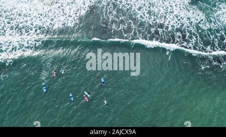 Vista aerea del surfer nuoto a bordo vicino enorme blu oceano onda nel Porto da Cruz, l'isola di Madeira, Portogallo Foto Stock