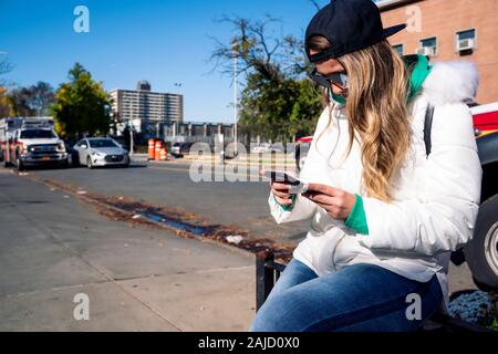 Attraente donna bionda seduta al sole con il suo smartphone Foto Stock