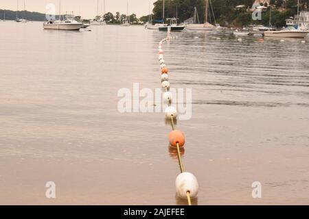 Un arancio e bianco corda cordoni off di un area nuoto presso una spiaggia nei pressi di barche. Foto Stock