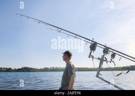 Le avventure di pesca, la pesca alla carpa. L'uomo la pesca sul lago con attrezzature moderne, vista laterale Foto Stock