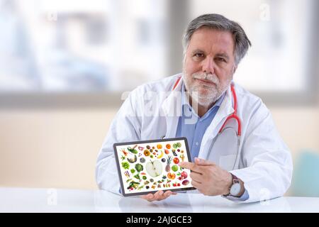 Medico nutrizionista holdingb tavoletta digitale.con verdura e frutta sullo schermo in ufficio Foto Stock