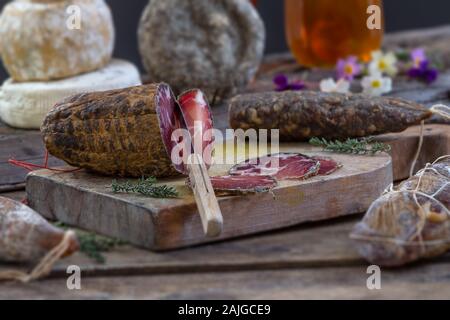 Diverse varietà di Corsica tradizionale di salumi con un ramo di olivo e olive nere su sfondo di legno. Foto Stock