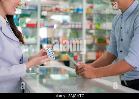 Fiducioso asiatici femmina giovane farmacista con un bel sorriso amichevole e spiegando le capsule medicina per il suo cliente in farmacia farmacia. Medici Foto Stock