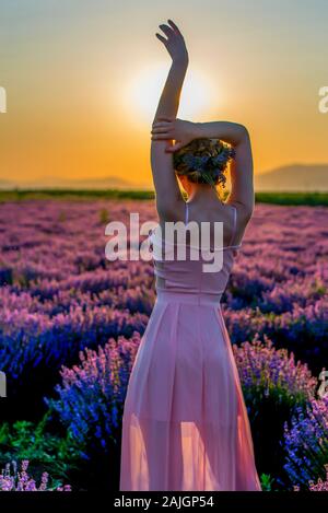 Una giovane donna passeggiando attraverso un campo di lavanda al tramonto, godendo di un bel momento in natura. Foto Stock