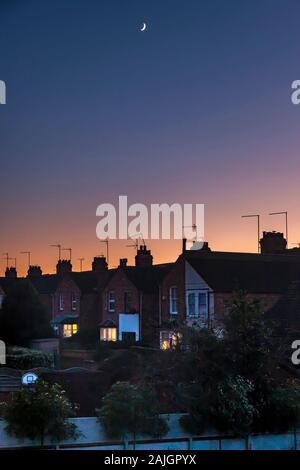 Northampton, Regno Unito. Cielo colorato appena dopo il tramonto sui tetti della Abington Area della città un affievolimento quarto di luna in alto nel cielo. Foto Stock