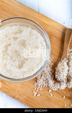 Riso ammollato, grano, acqua liquida torbida in ciotola di vetro su fondo di legno Foto Stock