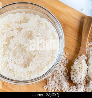 Riso ammollato, grano, acqua liquida torbida in ciotola di vetro su fondo di legno Foto Stock