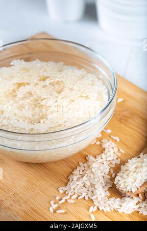 Riso ammollato, grano, acqua liquida torbida in ciotola di vetro su fondo di legno Foto Stock