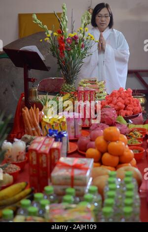 Un monaco femminile sta pregando davanti ad un altare con offerte. Foto Stock