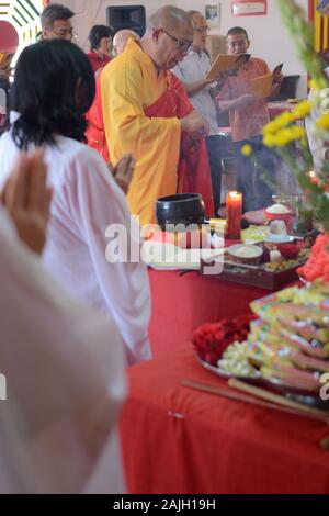 Un sacerdote buddista conduce una cerimonia di preghiera davanti ad un altare con offerte prima della celebrazione del Capodanno cinese. Foto Stock