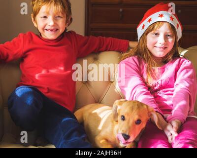 Kids in santa caps giocando con grazioso cucciolo Foto Stock