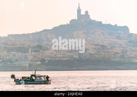 Piccola barca da pesca davanti a Notre Dame de la Garde cattedrale e lo skyline di Marsiglia, la baia di Marsiglia Provence, Francia Foto Stock