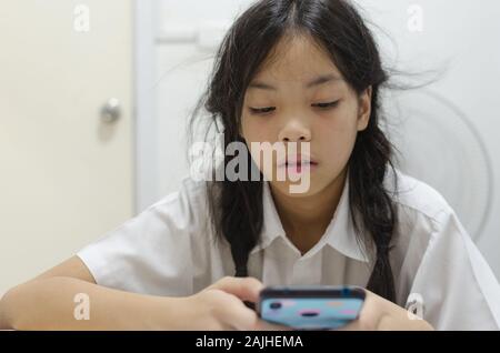 Giovani schoolgirl addicted a telefonino giochi. Fa di lui non è interessato a fare i compiti. Foto Stock