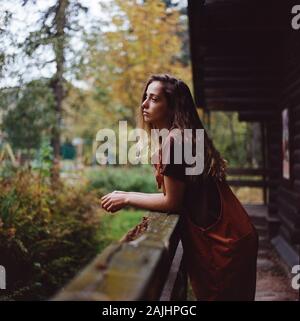 La donna è in piedi vicino alla vecchia casa in legno e guardando lontano Foto Stock