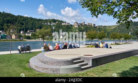 Un gruppo di turisti anziani si siedono sul lungomare lungo il fiume Might Rhine mentre attendono una nave della linea di crociera KD per fermarsi e portarli sul fiume. Foto Stock