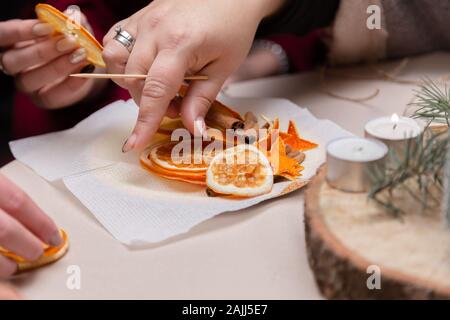 Le donne la mano facendo decorazioni da essiccato arance, stelle dal mandarino e cannella. Girls party o riunione. Foto Stock