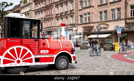 Il motore anteriore di un trolley turistico rosso e di un biciclo maschile sono visti sulla piazza acciottolata nel centro di Norimberga, in Germania Foto Stock