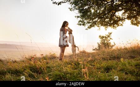 Adorabile ragazza giovane giocando in esecuzione con il suo simpatico cane sulla natura durante il tramonto Foto Stock