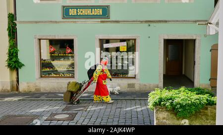 Uomo vestito con un abito a pagliaccio colorato che tira i bagagli insieme al suo fidato cane nella città medievale di Rothenburg, in Germania. Foto Stock