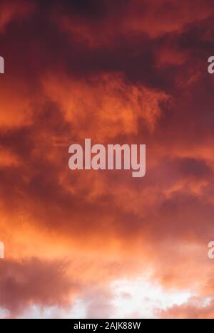 Nuvole temporalesche cattura il rosso e arancione bagliore del sole Foto Stock