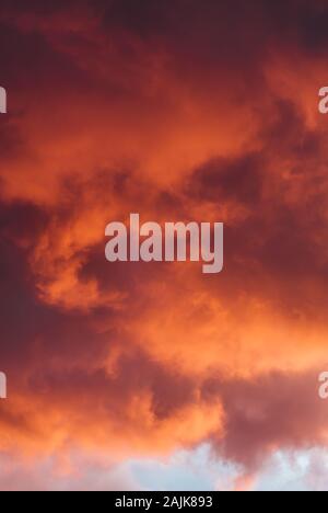 Nuvole temporalesche cattura il rosso e arancione bagliore del sole Foto Stock