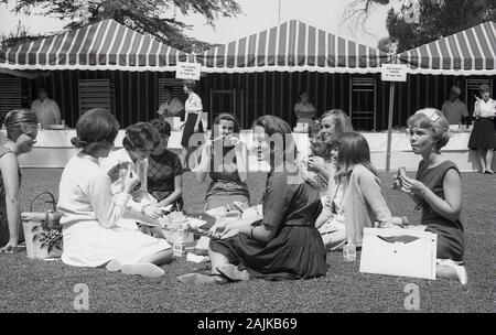 1964, studenti storici, nuove donne seduti fuori sul prato in un campus universitario che pranzano, California, USA. Foto Stock