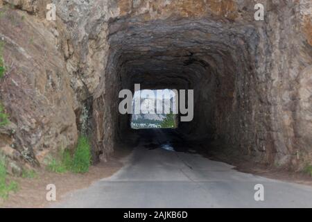 La singola corsia Doane Robinson tunnel su Iron Mountain Road con segnali di attenzione e di una vista del monte Rushmore in background. Foto Stock