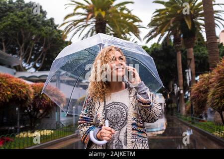 Attraente e allegro fashion alla moda di mezza età giovane donna caucasica passeggiate in città sotto la pioggia con un ombrello trasparente - Stagione fredda c Foto Stock