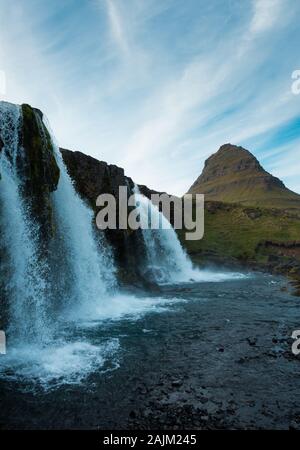 Famose cascate islandese con incombente Kirkjufell arrowhead mountain in background. Cielo blu e nuvole sopra, shot sulla giornata di sole. N. persone visibili. Foto Stock