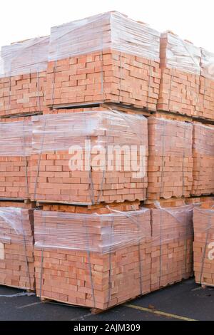 Diversi pallet con mattoni di cemento sovrapposti in magazzino. La produzione industriale di mattoni. foto verticale. Foto Stock